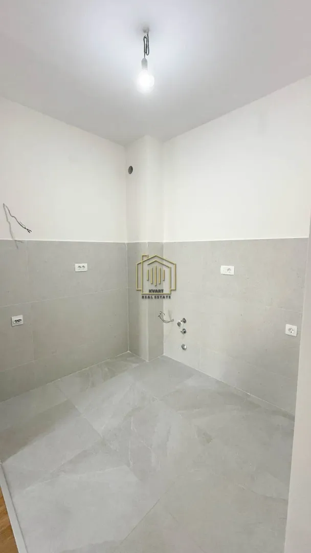Prazna prostorija sa pločicama na donjem dijelu zidova i pripremljenim instalacijama.