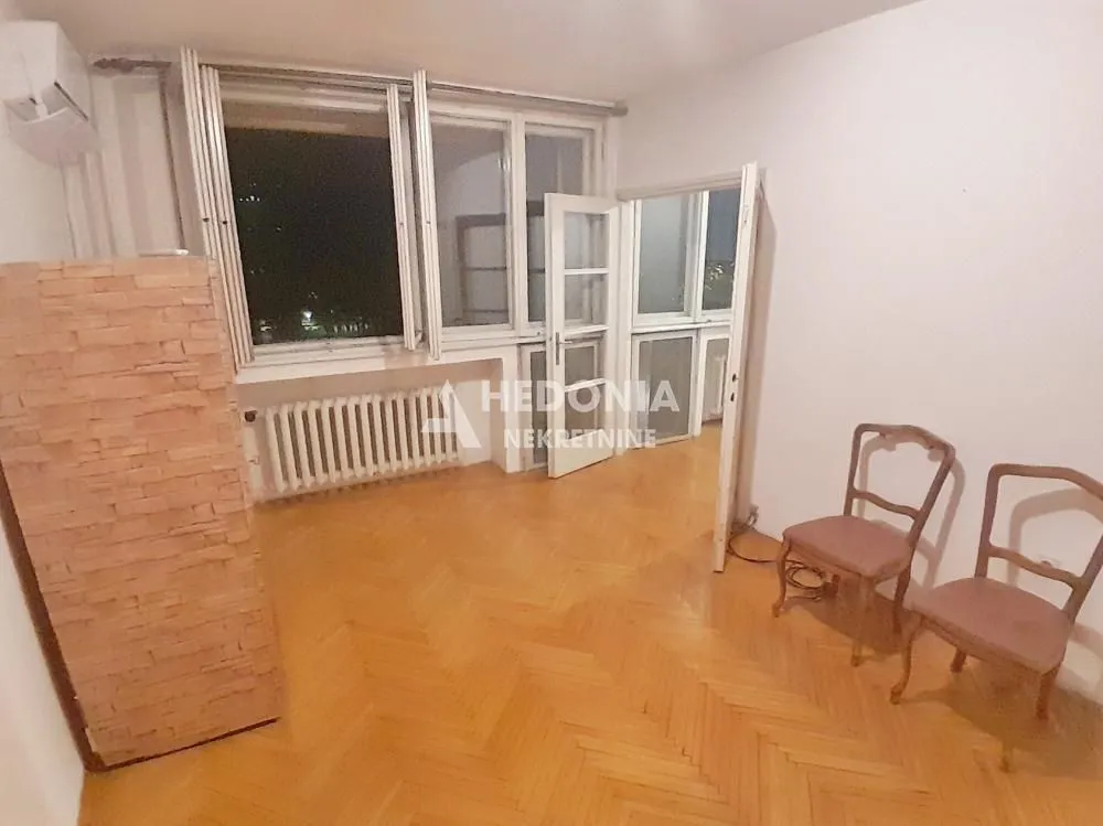 Empty room with hardwood parquet flooring, large windows, and double doors.