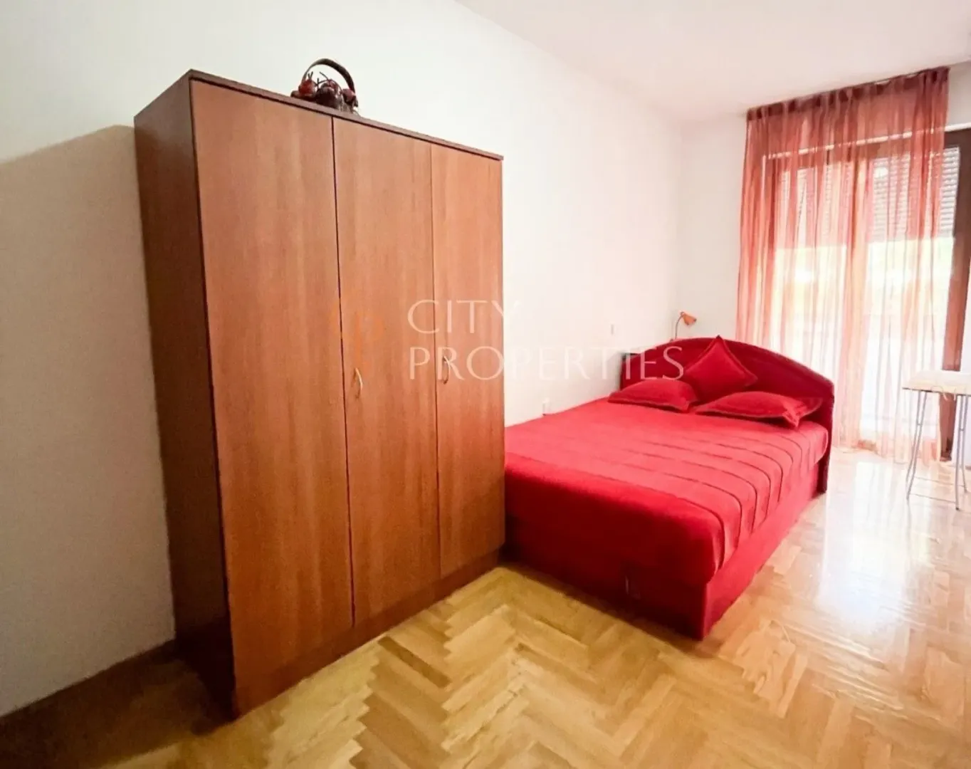 Bright bedroom featuring a red bed and a wooden wardrobe.