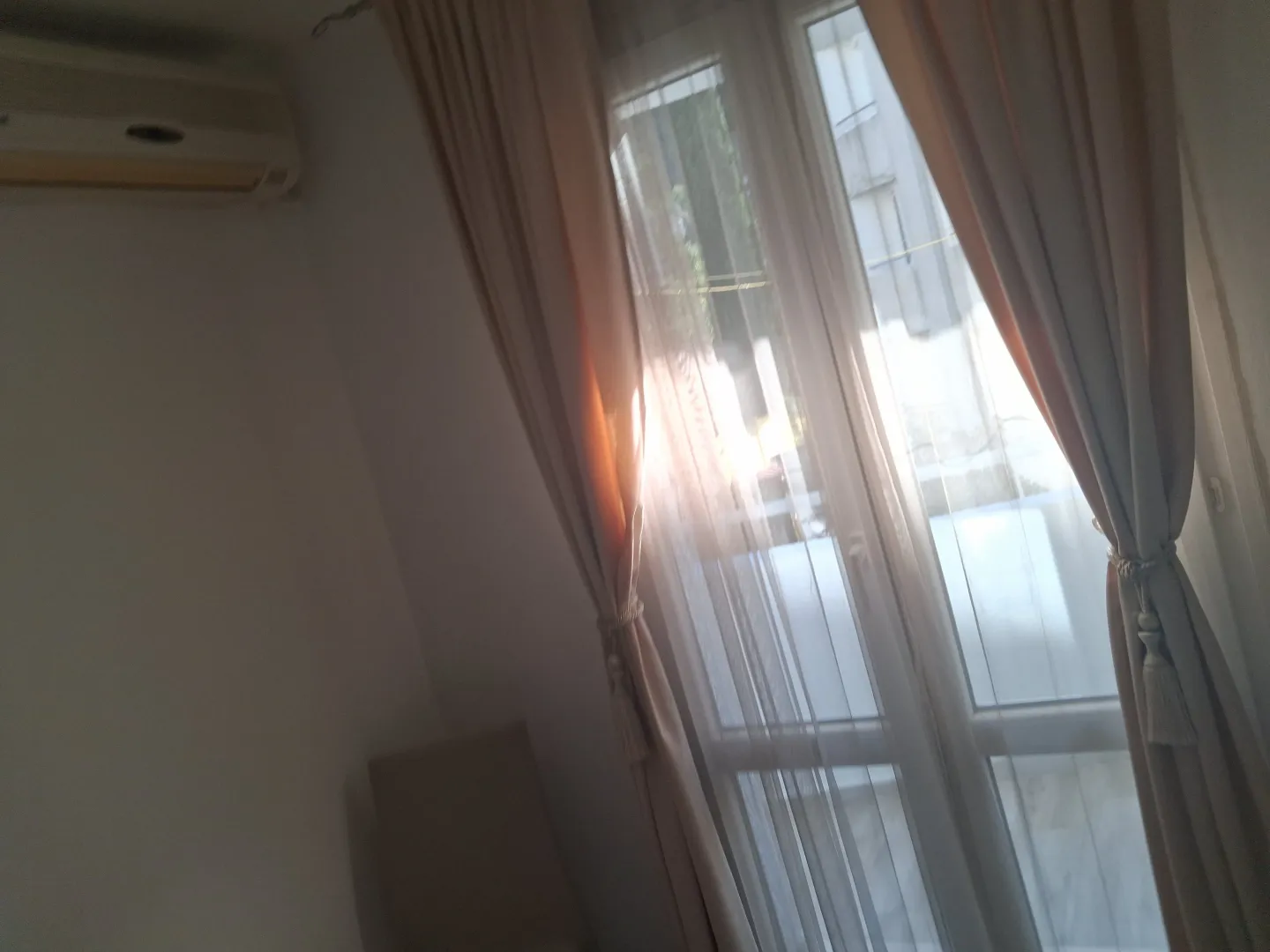 View of a window with curtains and an air conditioning unit on the wall.