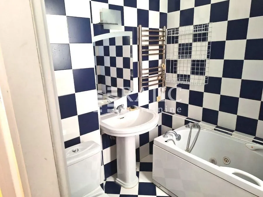 Manje kupatilo sa kadom, umivaonikom i wc šoljom, obloženo crno-belim pločicama.