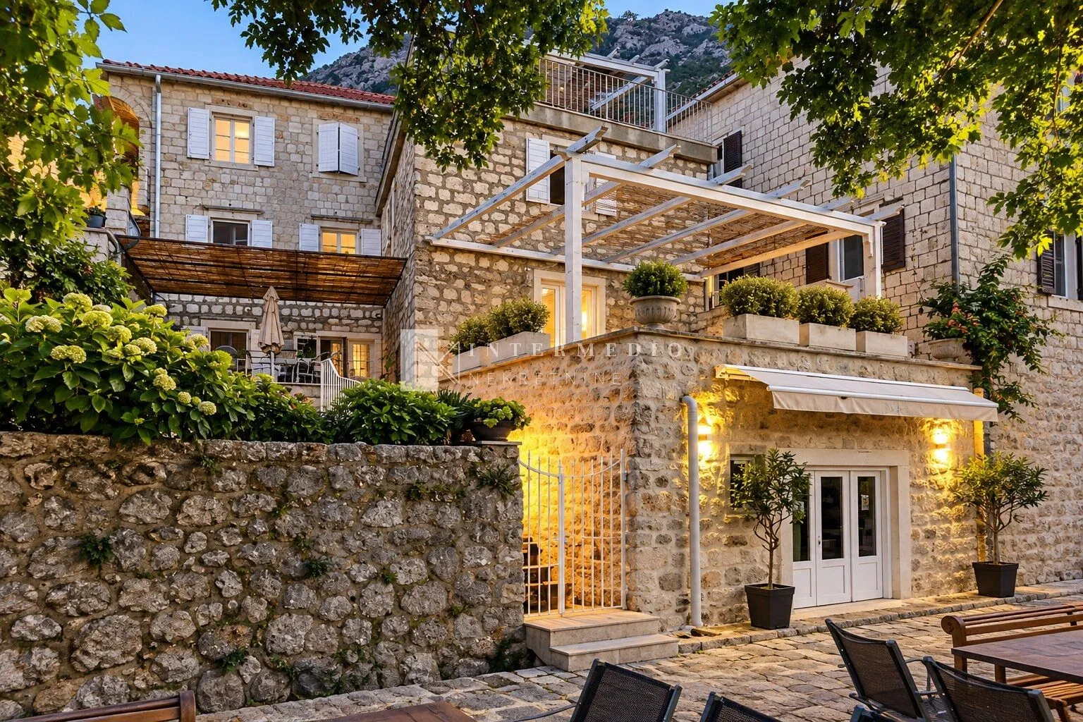 Eksterijer tradicionalne kamene kuće sa terasom i uređenim dvorištem.