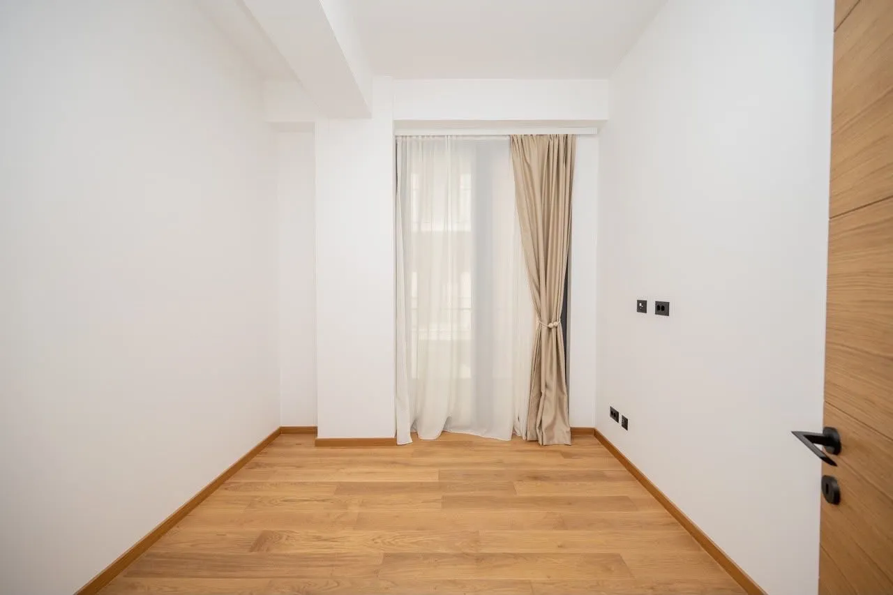 Empty bright room with parquet flooring and a window covered with curtains.