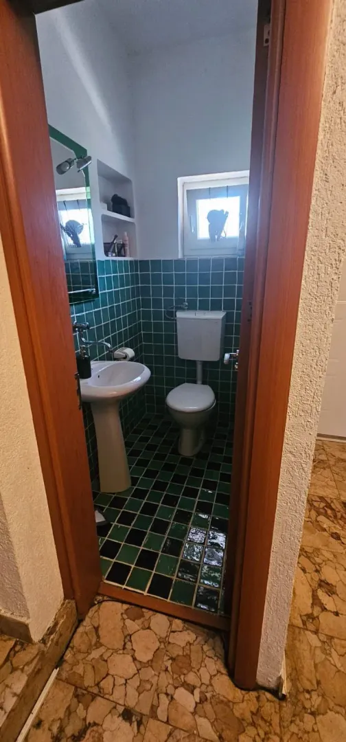 A view through the door into a bathroom with green tiles, a sink, and a toilet.