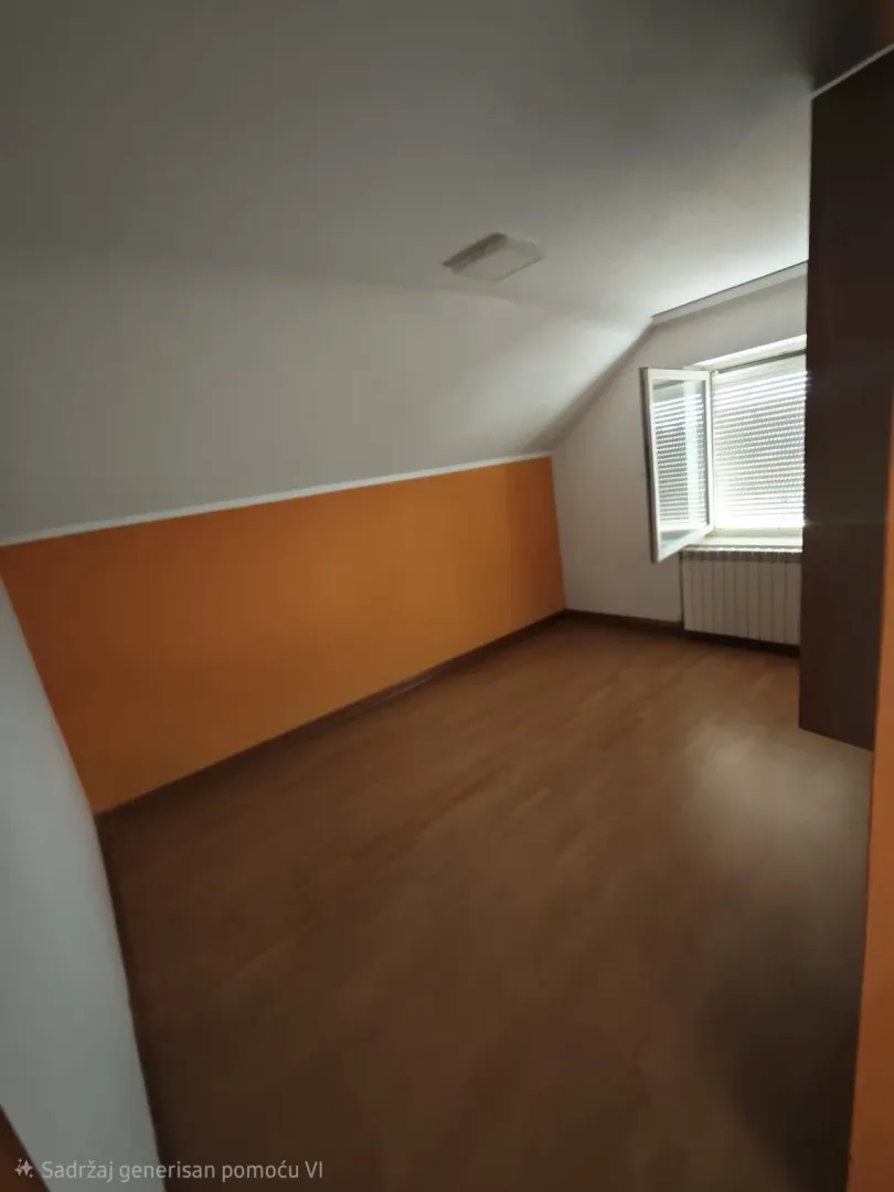 Prazna soba sa kosim plafonom i narandžastim zidom.