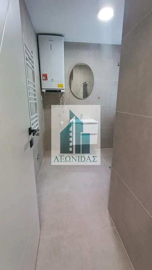 Pogled na kupatilo obloženo keramičkim pločicama sa umivaonikom, ogledalom i bojlerom.
