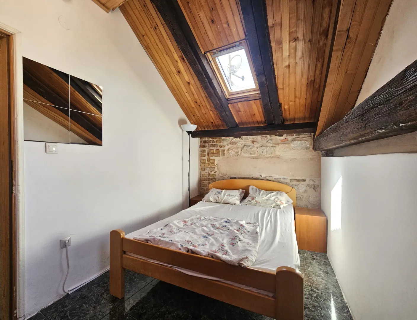 Attic bedroom with wooden roof beams, a skylight, and a double bed.