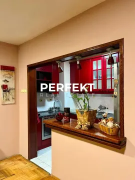 Pogled na kuhinju sa crvenim elementima kroz šank sa drvenom radnom površinom. - image 6