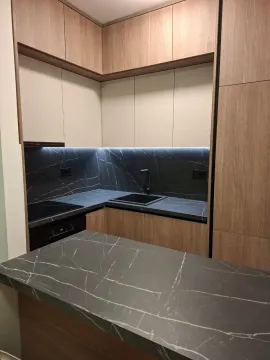 Moderna kuhinja sa drvenim elementima, tamnim radnim površinama i ugrađenim osvjetljenjem. - image 5
