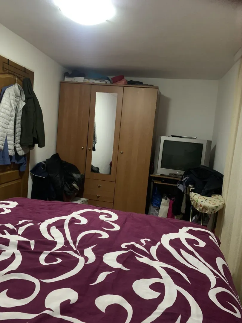 A bedroom with a wooden wardrobe, a television, and a bed in the foreground.
