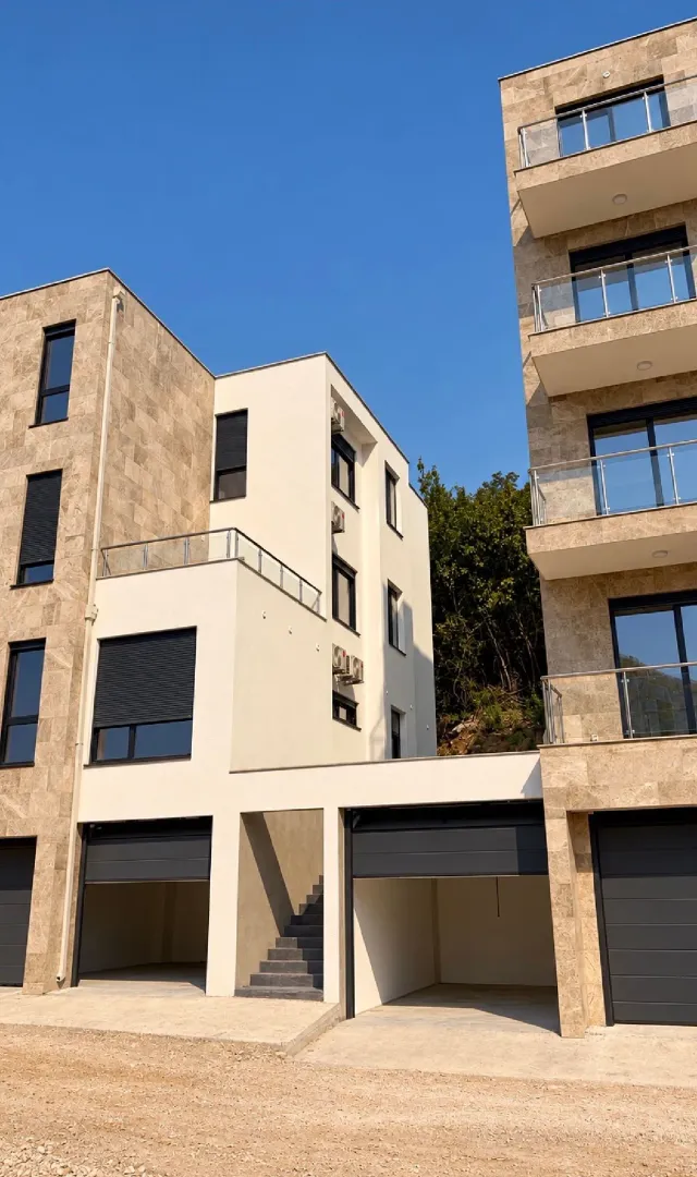 Pogled na spoljašnjost moderne stambene zgrade sa garažama u prizemlju.