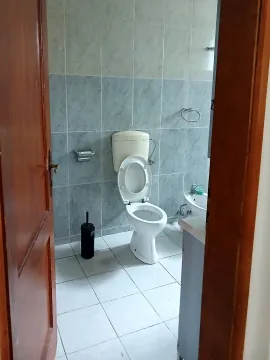 View of the tiled bathroom with a toilet bowl through the open door. - image 3
