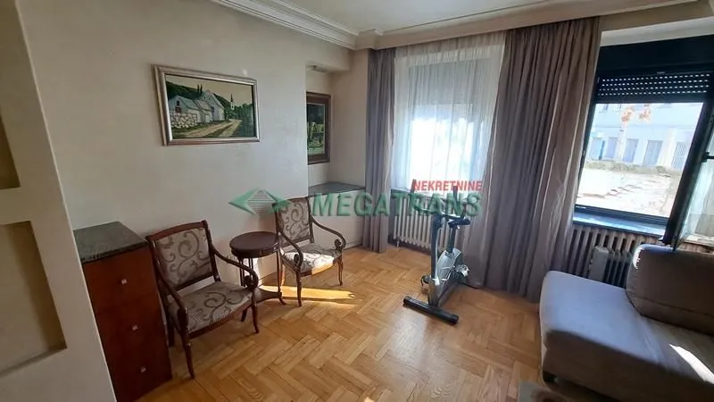 Dnevna soba sa garniturom, foteljama i sobnim biciklom pored prozora.
