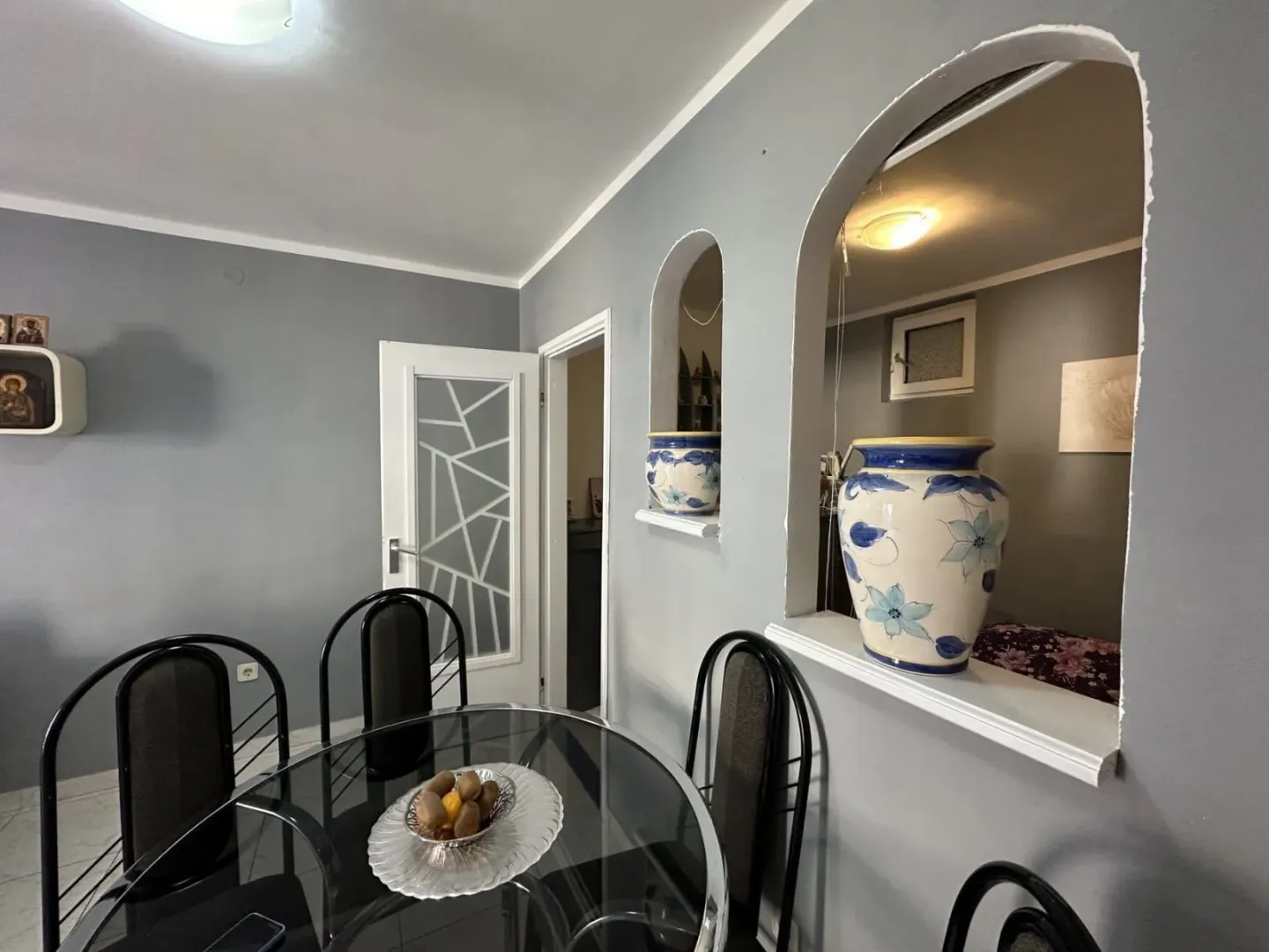 Dining area with a glass table and decorative vases on the partition wall.