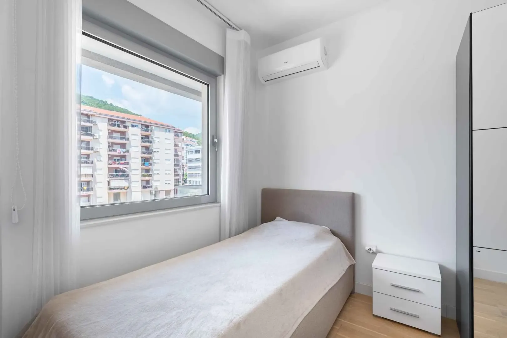 Small bedroom with a bed, white nightstand, and air conditioning unit.