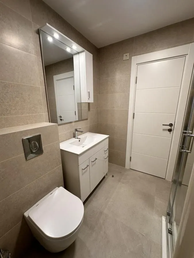 Moderno kupatilo sa tuš kabinom, umivaonikom i ugrađenom wc šoljom.