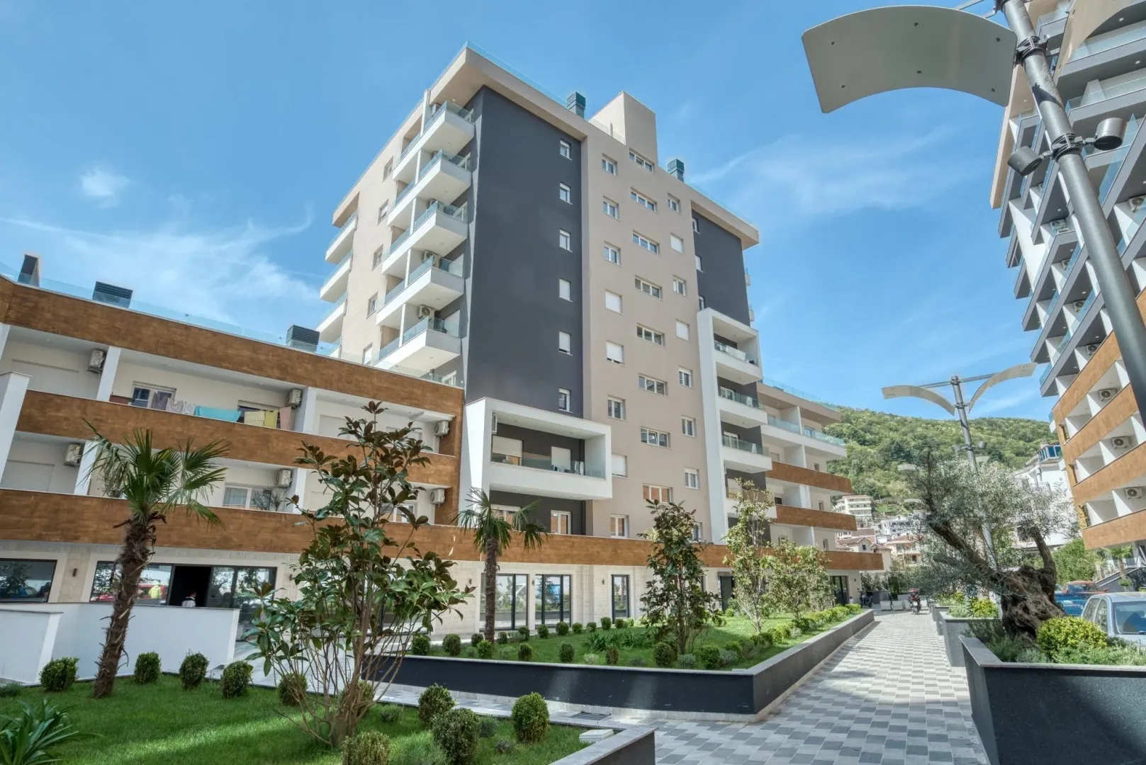 Spoljašnji izgled moderne stambene zgrade sa uređenim dvorištem.