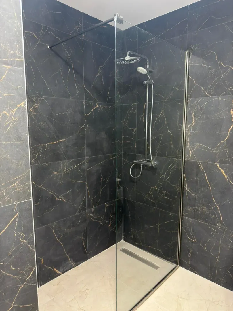 Moderno kupatilo sa tuš kabinom i crnim pločicama sa zlatnim šarama.