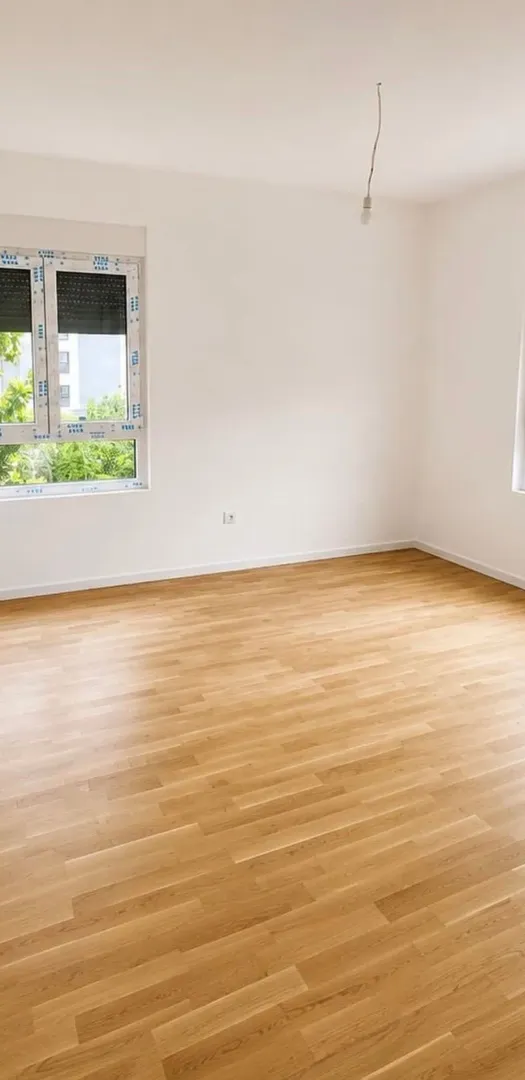 Prazna soba sa parketom i bijelim zidovima.