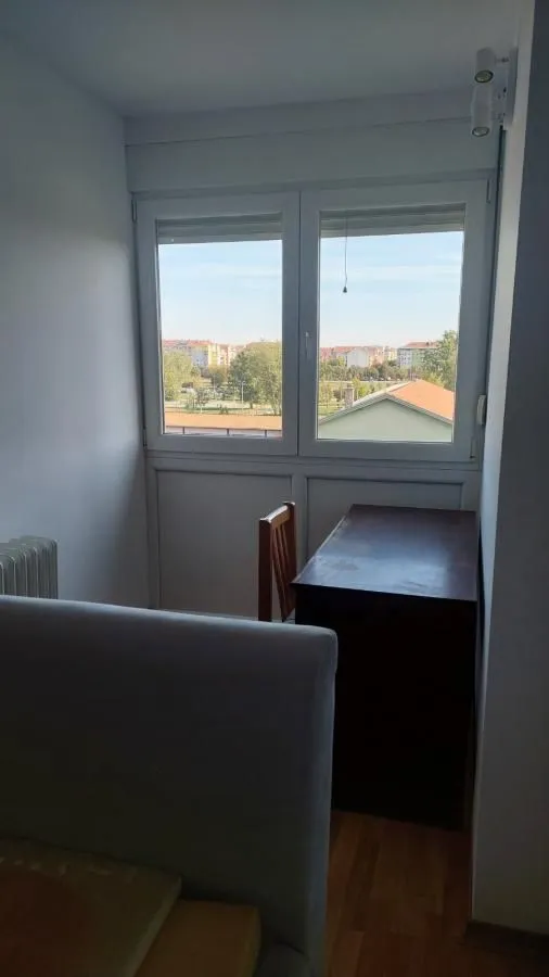 Manja spavaća soba sa krevetom, radnim stolom i prozorom sa pogledom na naselje.