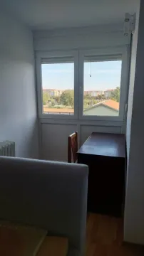 Manja spavaća soba sa krevetom, radnim stolom i prozorom sa pogledom na naselje. - image 8