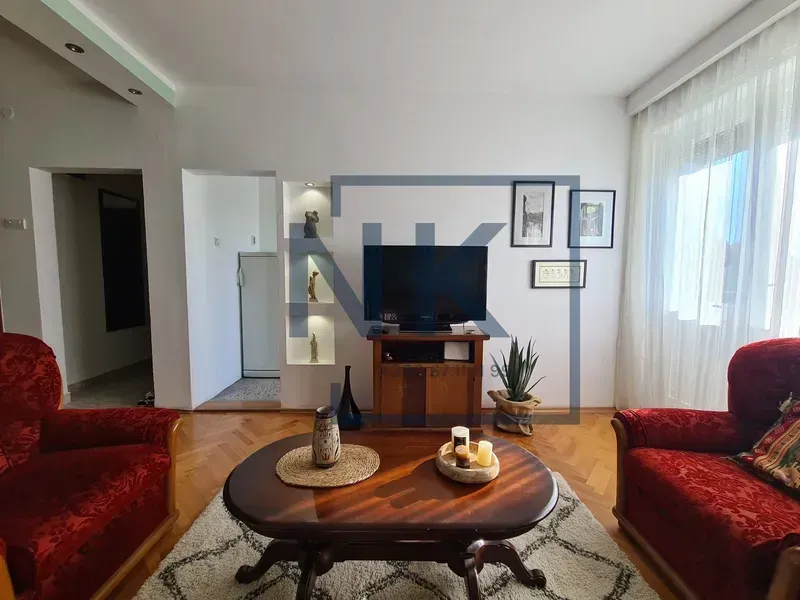Dnevna soba sa crvenim foteljama, televizorom i drvenim stočićem.