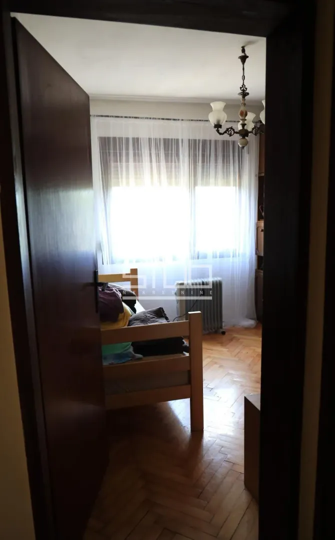 View from the hallway into a bedroom with a wooden bed and parquet flooring.
