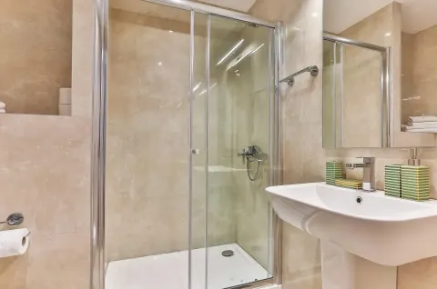 Bathroom equipped with a shower cabin, washbasin, and mirror with beige tiles. - image 5