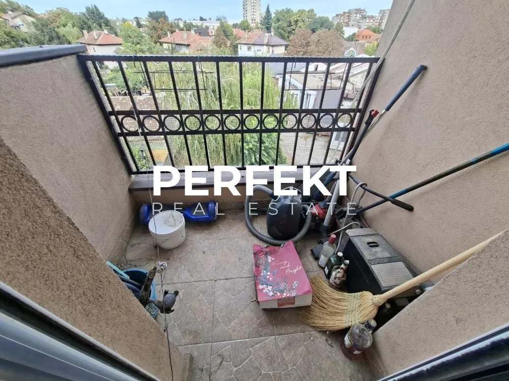 Manji popločani balkon sa metalnom ogradom i odloženim kućnim potrepštinama.
