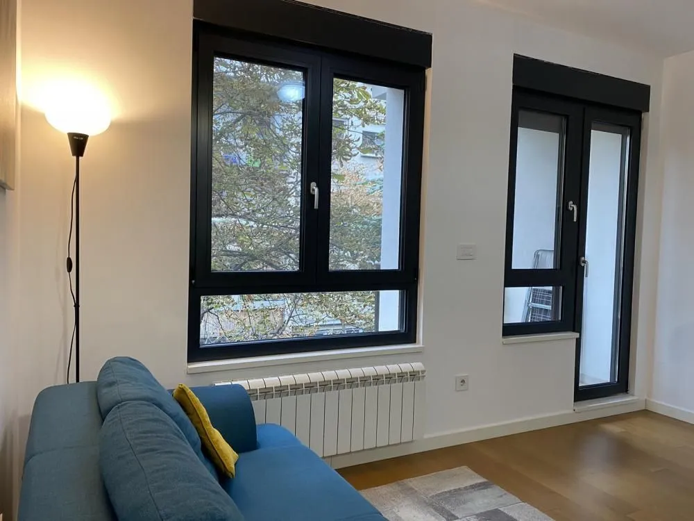 Living room with a blue sofa, large windows and parquet flooring.