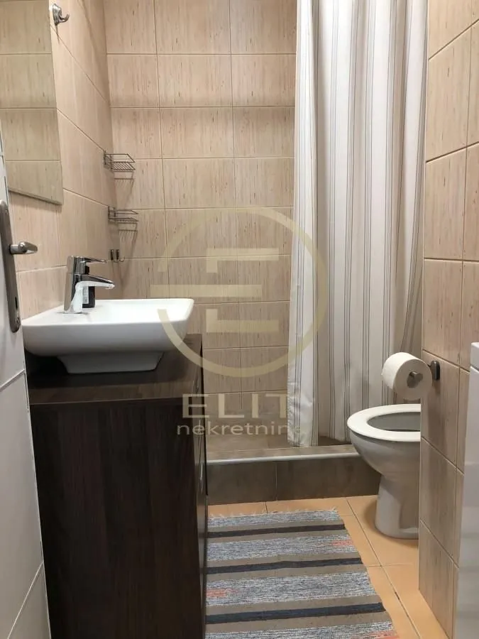 Kupatilo opremljeno umivaonikom, WC šoljom i tuš kabinom sa zavesom.