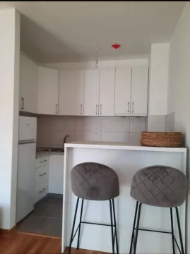 Mala, moderna bijela kuhinja sa šankom i dvije sive barske stolice. - image 4