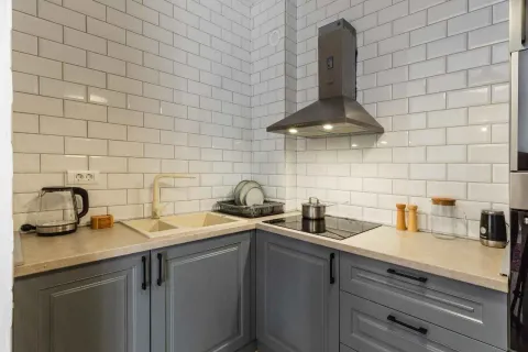 Kitchen equipped with grey cabinets, white tile backsplash, and a built-in cooktop with a range hood. - image 9
