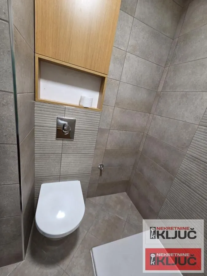 Pogled na kupatilo sa WC šoljom i zidnim ormarićem.