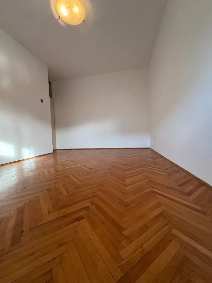 Prazna soba sa parketom i bijelim zidovima.