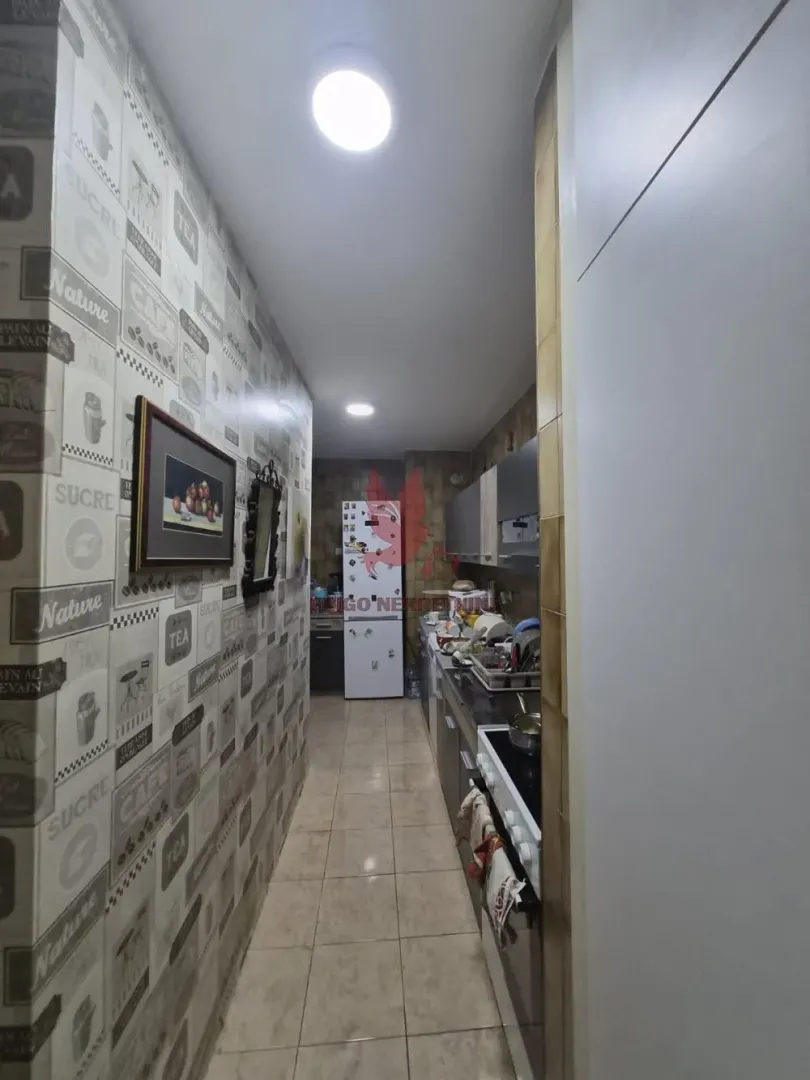 Ugaoni pogled na usku kuhinju sa elementima i frižiderom na kraju.