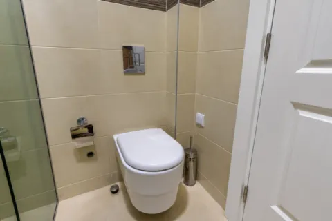 Pogled na moderno opremljenu toaletu sa konzolnom šoljom i bež pločicama. - image 10