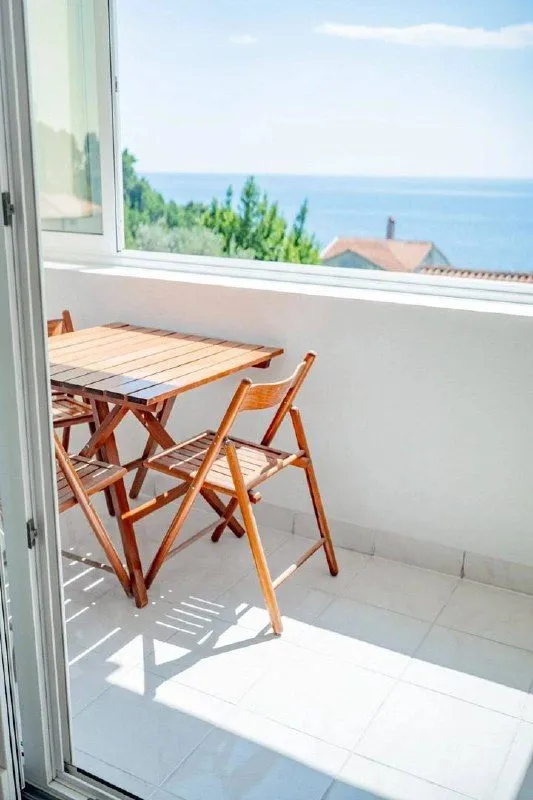 Svijetli balkon sa drvenim stolom i stolicama i pogledom na more.