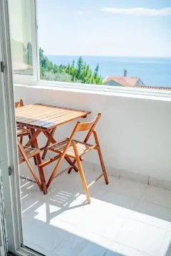 Svijetli balkon sa drvenim stolom i stolicama i pogledom na more. - image 4