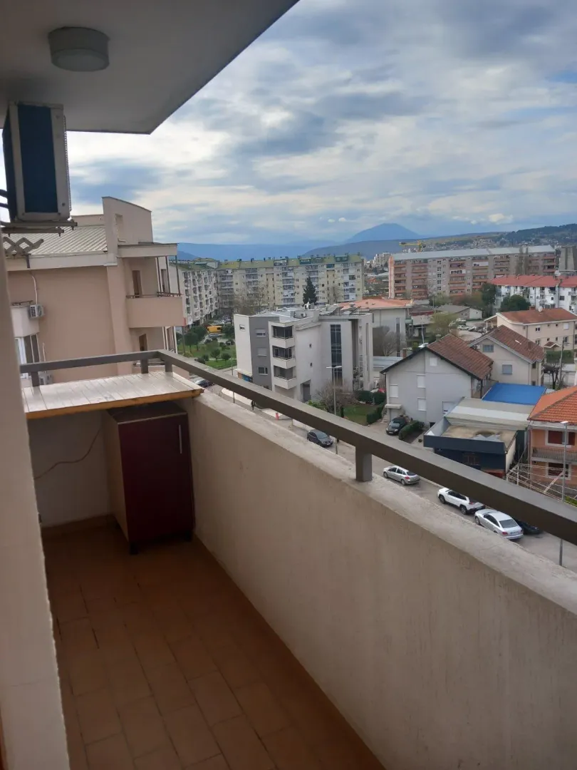 Pogled sa balkona na okolne zgrade i planine u daljini.