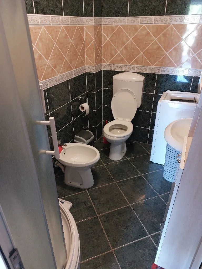 Kupatilo sa wc šoljom, bideom, umivaonikom i pločicama u zelenim i bež tonovima.