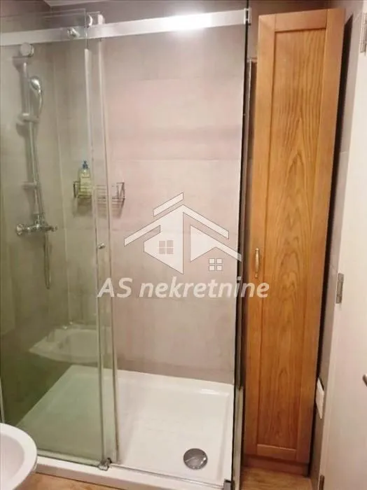 Kupatilo sa tuš kabinom i drvenim ormarićem.