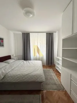 Svetla spavaća soba sa bračnim krevetom, belim elementima i prozorom sa zavesama. - image 6