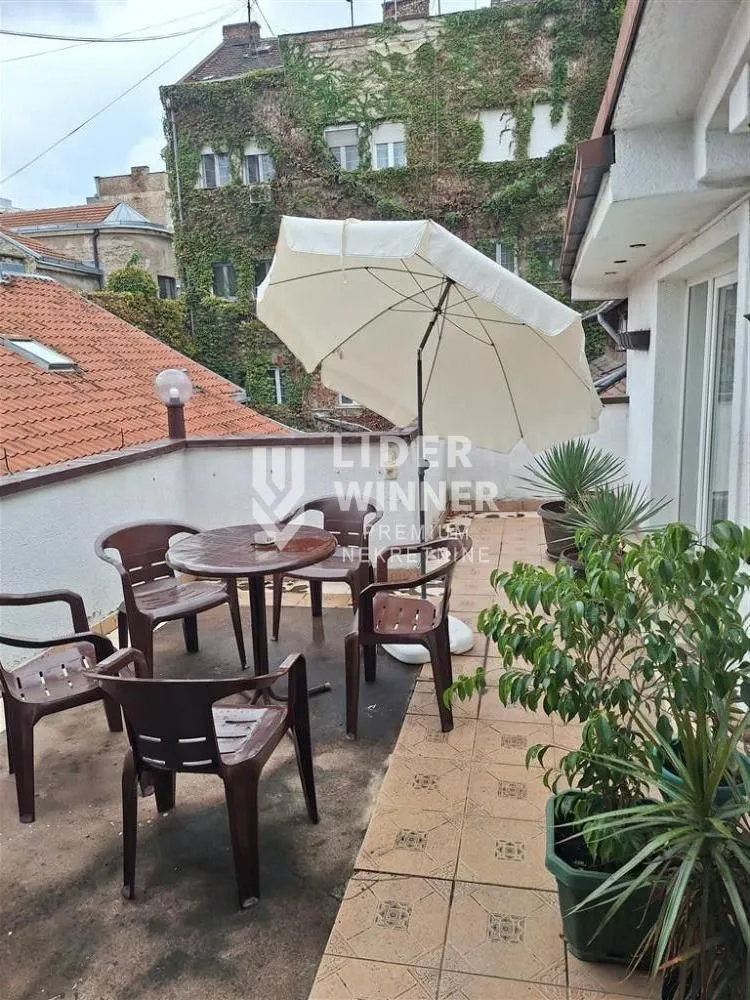 Terasa sa garniturom za sedenje, suncobranom i saksijama sa biljkama.
