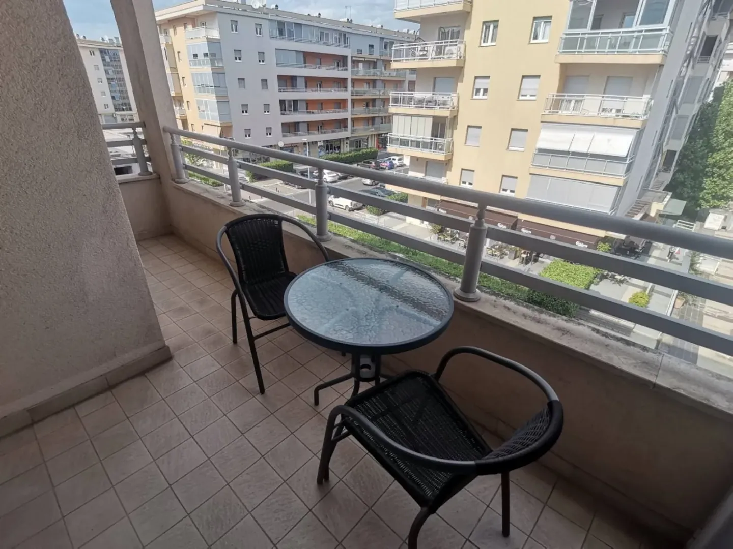 Balkon sa stolom, dvijema stolicama i pogledom na okolne zgrade.
