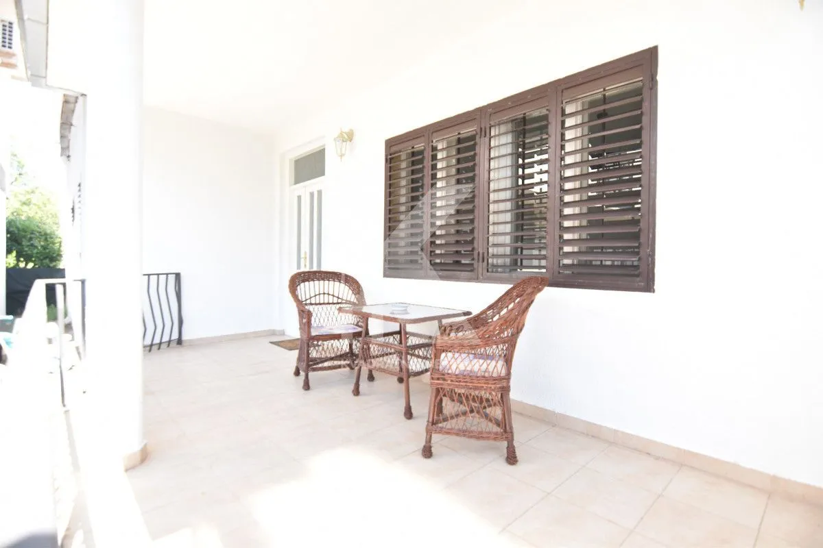 Covered terrace with wicker furniture and windows with shutters.