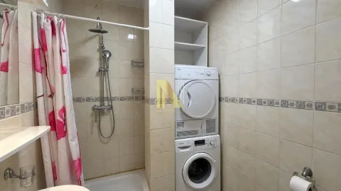 Kompaktno kupatilo sa tuš kabinom, belim pločicama i ugrađenom mašinom za veš i sušenje. - image 9