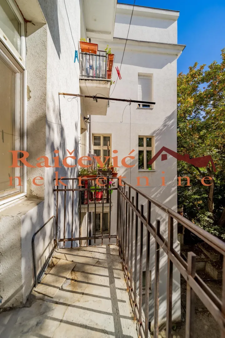 Manji balkon sa metalnom ogradom i pogledom na dvorište zgrade.