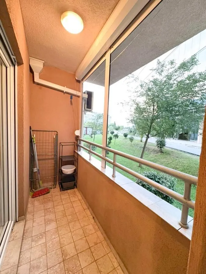 Manji zatvoreni balkon sa pogledom na zelenilo i drveće ispred zgrade.