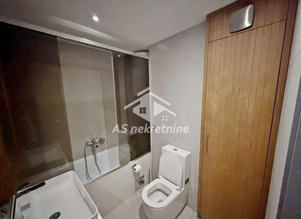 Modernly equipped bathroom with a bathtub, washbasin, toilet, and built-in wardrobe.
